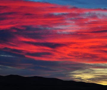 Photo of a dramatic red sunset with huge crimson clouds above dark mountains
